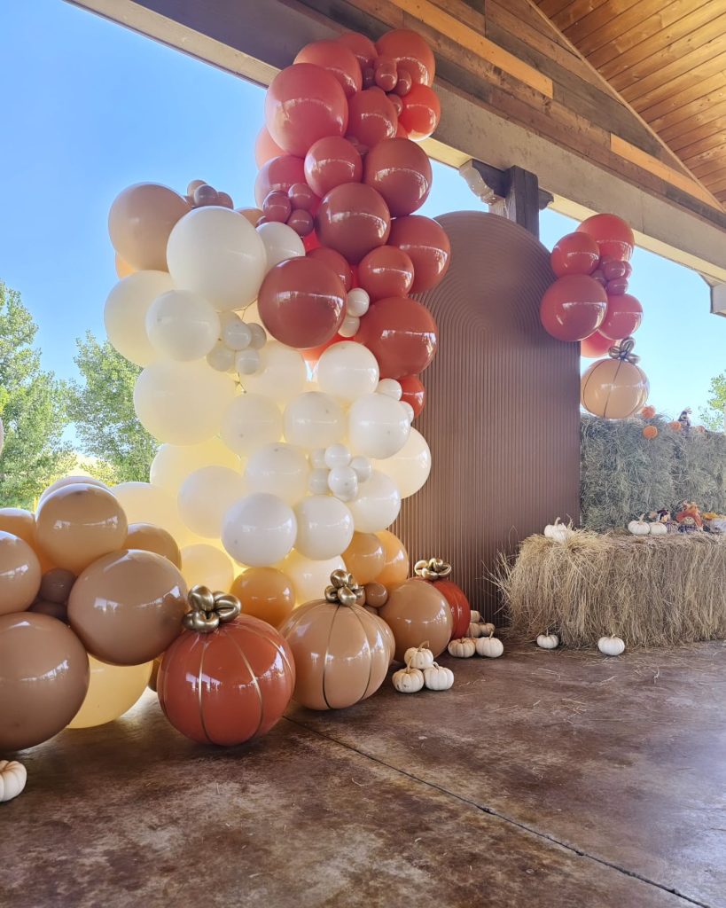 Autumn wedding decoration with balloon garland in warm tones, pumpkin shapes, and hay bale display