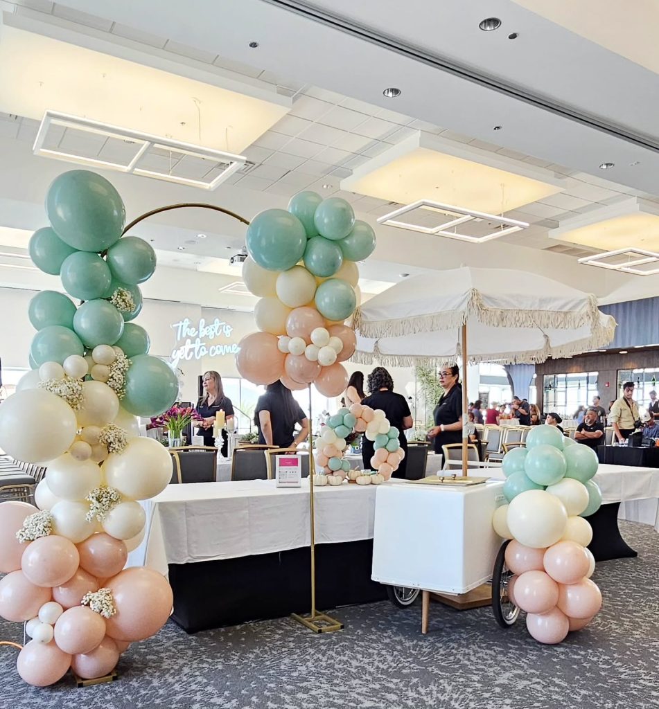Elegant balloon arch in mint green, gold, and blush pink surrounding white modern lounge furniture at indoor event