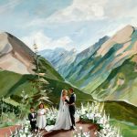 Painted mountain wedding ceremony with bride and groom exchanging vows among white floral arrangements and Colorado peaks