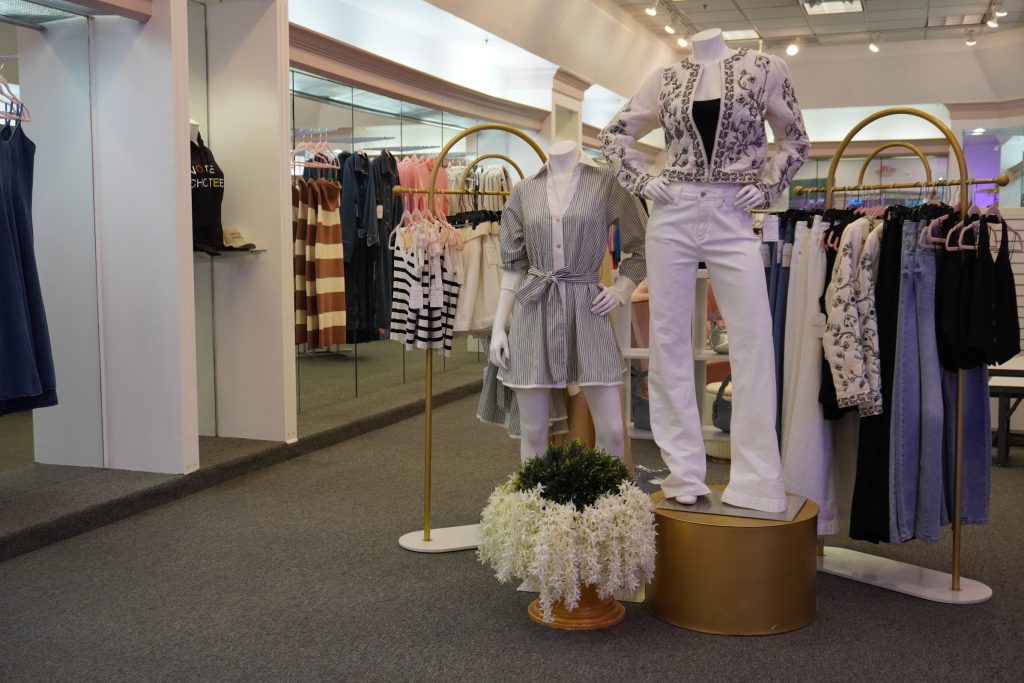 Modern boutique interior with gold display fixtures, mannequins in lavender outfits, and curated clothing racks