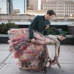 Couple in formal attire dancing on urban rooftop with downtown Indianapolis skyline in background