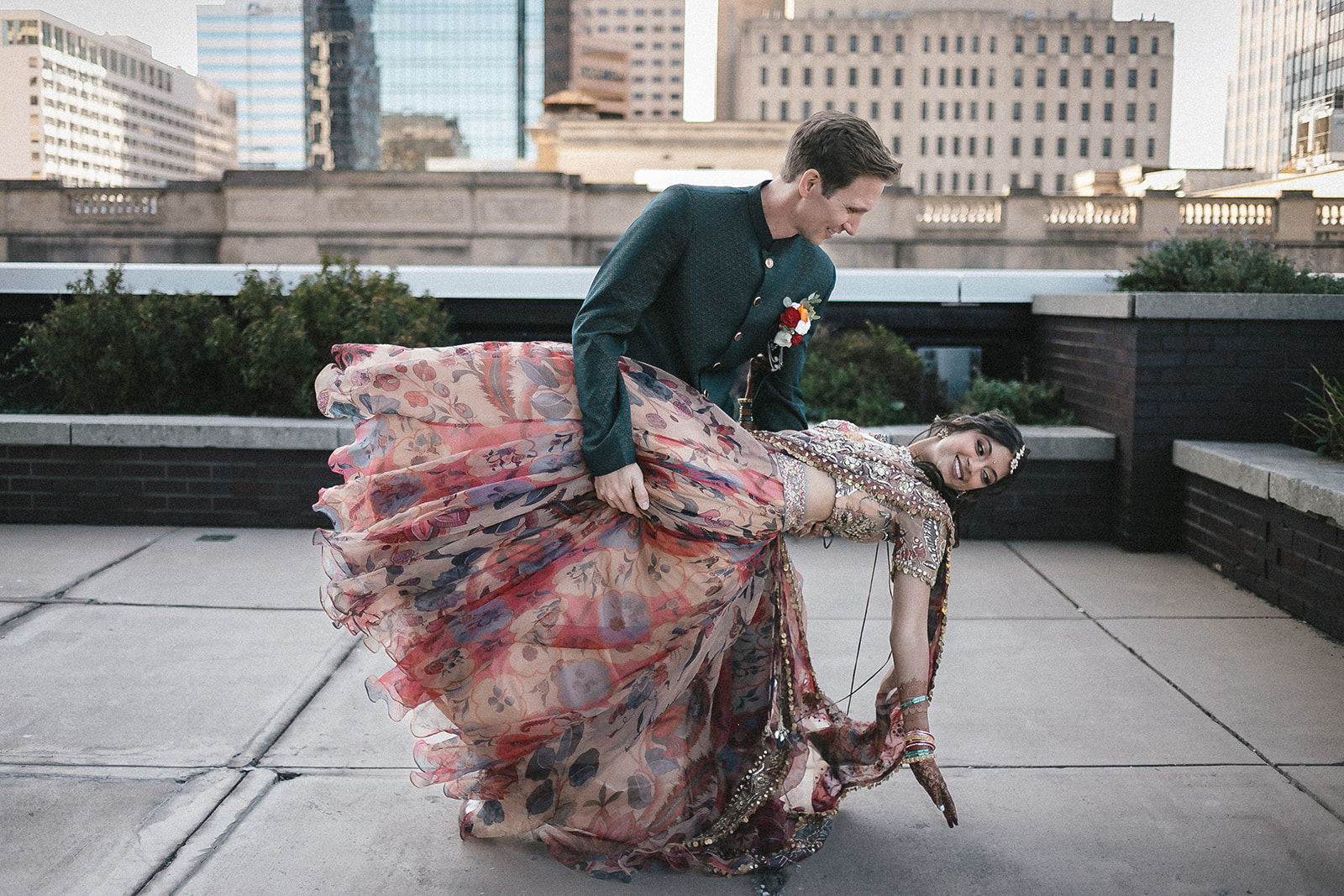Couple in formal attire dancing on urban rooftop with downtown Indianapolis skyline in background