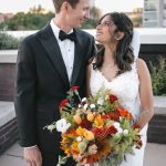Newlyweds sharing an intimate moment on rooftop terrace with vibrant autumn bouquet at sunset