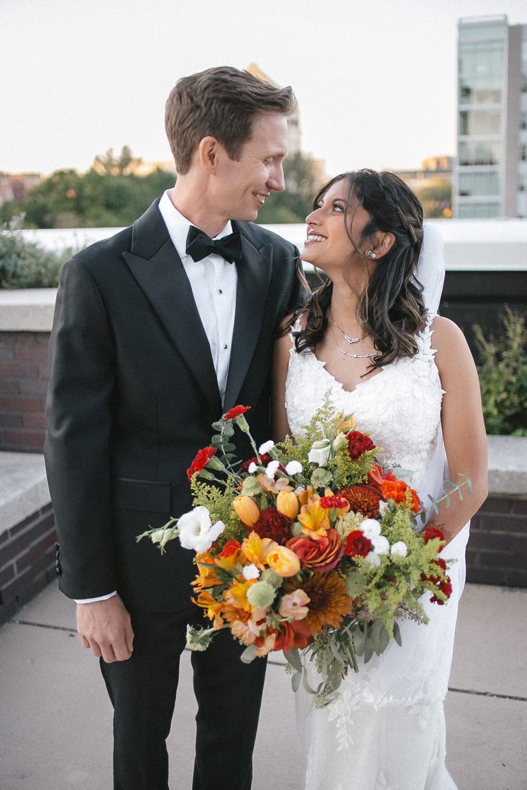 Newlyweds sharing an intimate moment on rooftop terrace with vibrant autumn bouquet at sunset