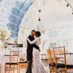 Couple sharing first dance under dramatic glass atrium ceiling with gold chiavari chairs