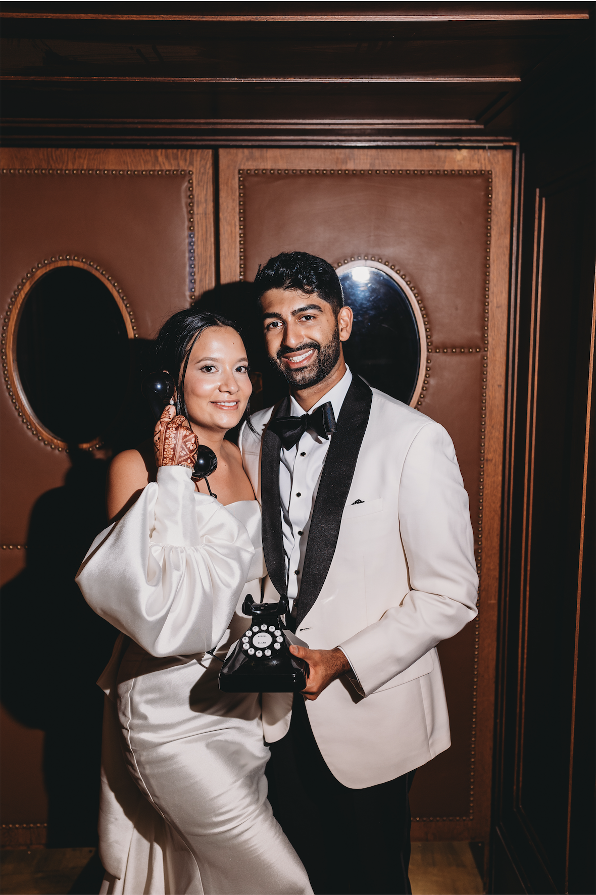 Bride and groom posing with vintage rotary telephone against art deco wood paneling