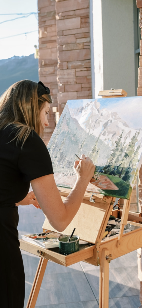 Kelsey Shields painting snowy mountain landscape on easel at outdoor venue