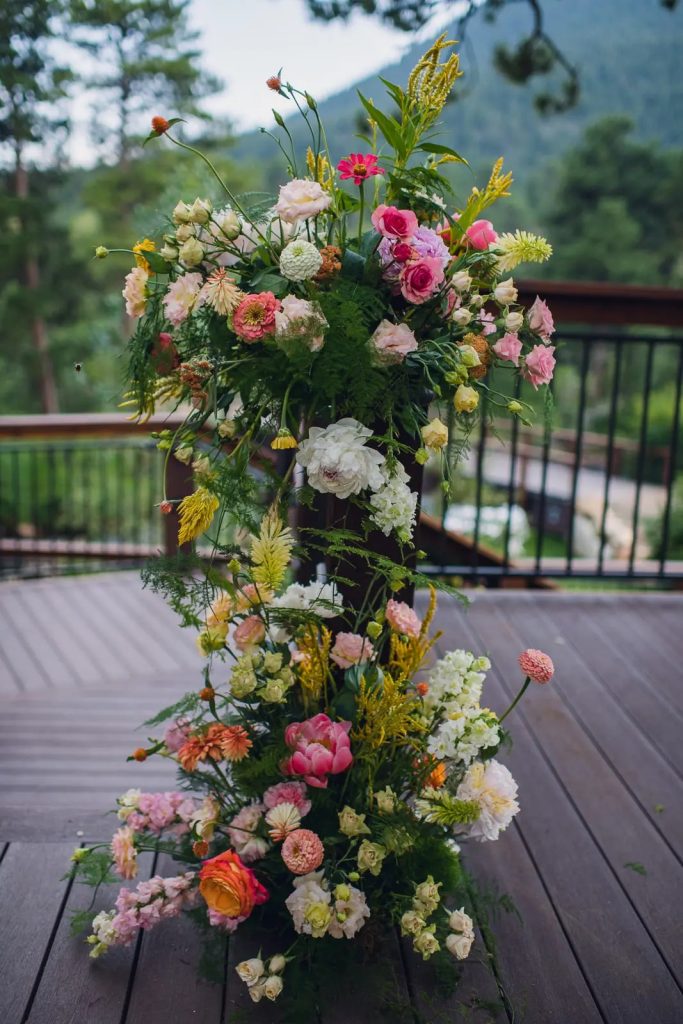 Tiered wedding floral arrangement with pink roses, white blooms, and yellow accents on mountain deck in Estes Park