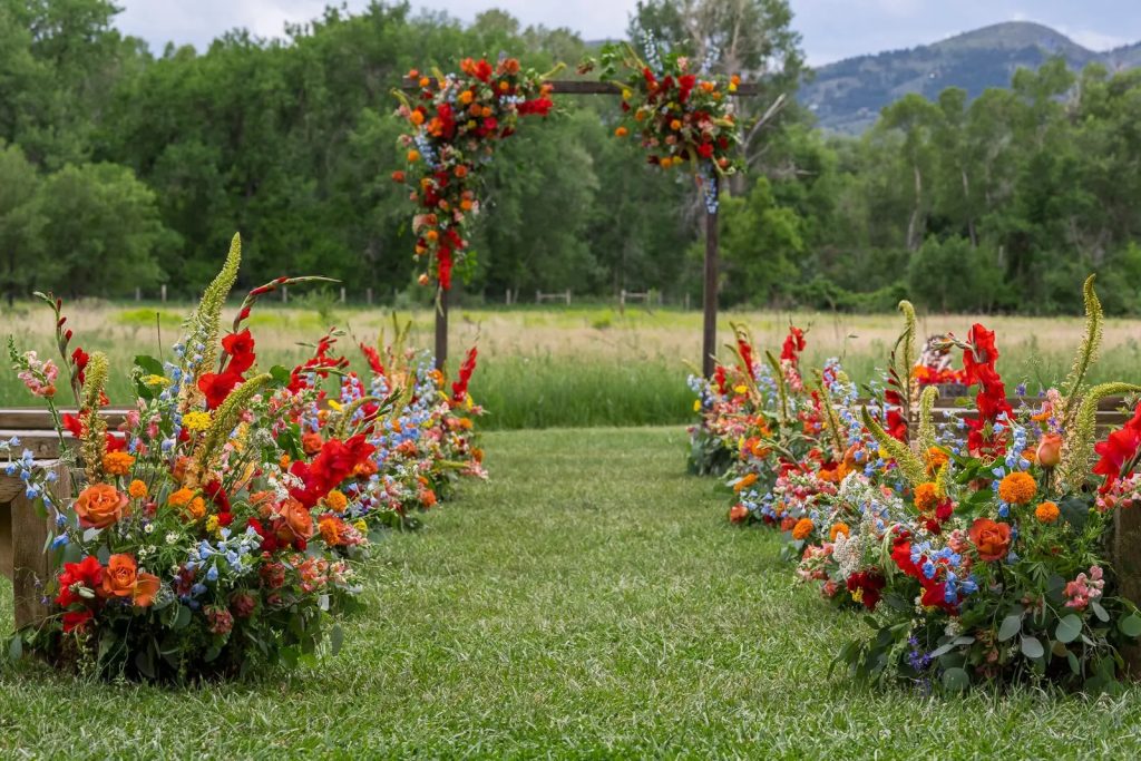 Outdoor wedding ceremony setup with vibrant red, orange, and blue floral arrangements flanking a ceremony arch