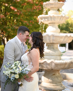 Bride and groom embrace near tiered fountain in outdoor garden setting