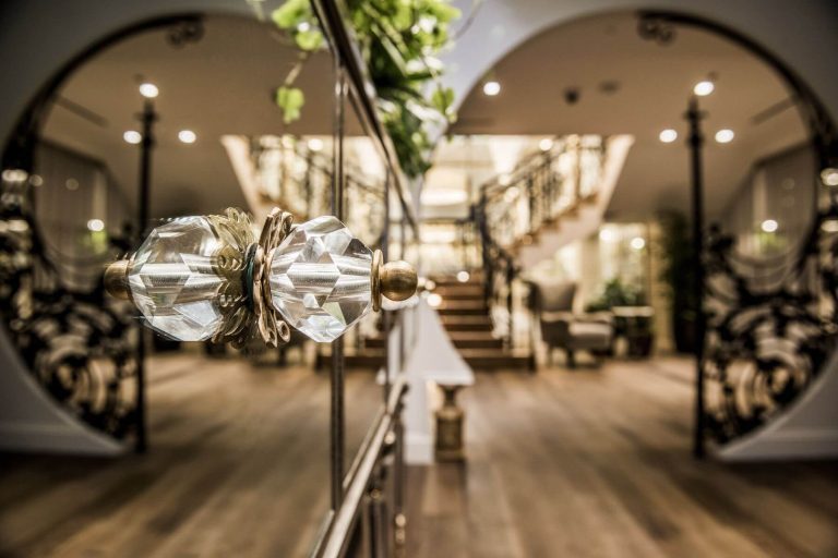 Ornate crystal door handle with brass accent leading into elegant hotel lobby with grand staircase