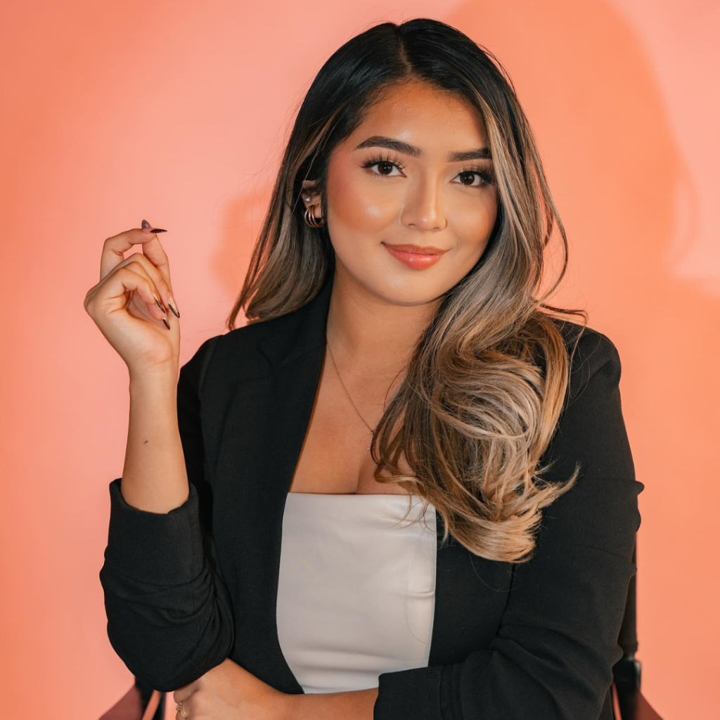 Portrait of JJ Beauty makeup artist in black blazer against coral background