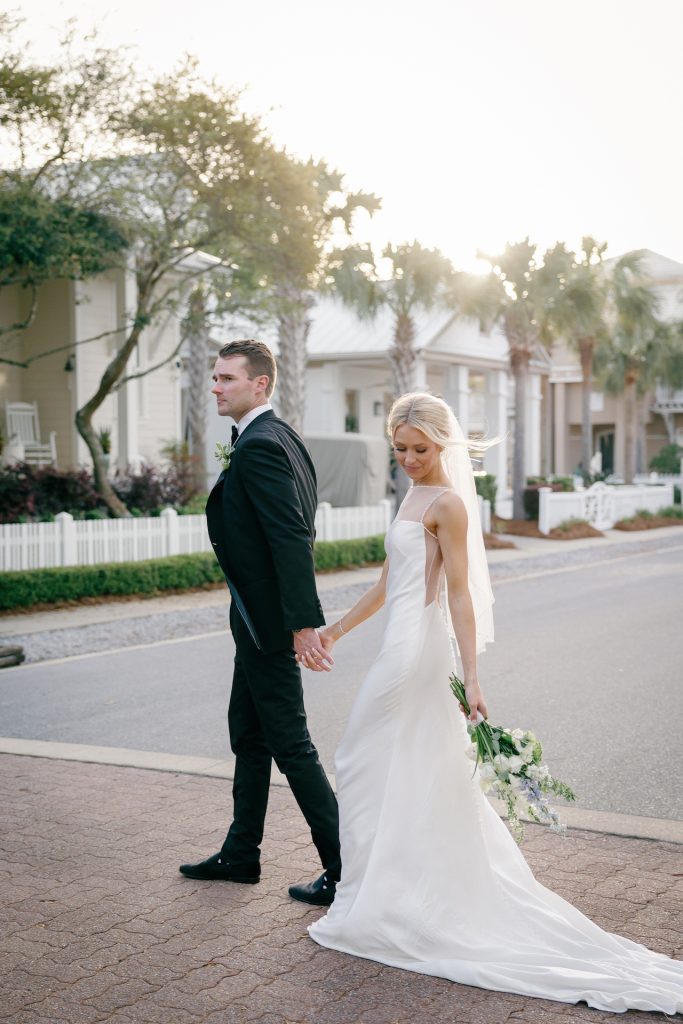Newlyweds walking hand-in-hand on residential street, bride holding cascading bouquet