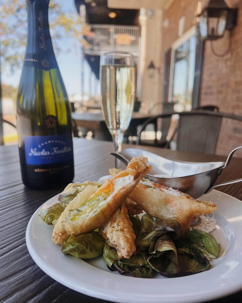 Champagne bottle and flute with fried appetizers and Brussels sprouts on outdoor patio dining table