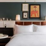 Elegant hotel room with white bedding, teal walls, and vintage elephant artwork at Perry Lane Hotel