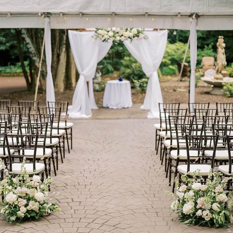 Outdoor wedding ceremony setup with white draped altar, chiavari chairs, and white rose arrangements