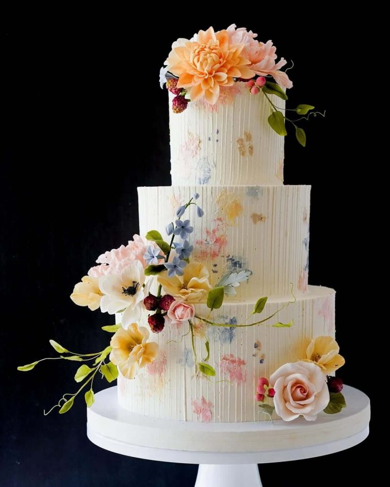 Four-tier white wedding cake with watercolor brushstrokes, vertical texture, and sugar flowers in peach, pink, and blue tones