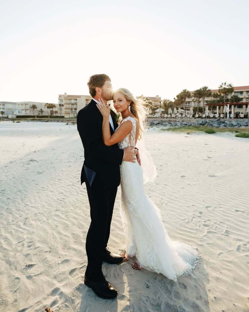 Newlyweds embracing on Savannah beach at sunset with palm trees and resort buildings in background