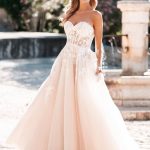 Bride in blush ball gown wedding dress with lace bodice and strapless sweetheart neckline by fountain