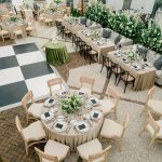Elegant tented wedding reception with checkerboard dance floor, round and rectangular tables, white floral arrangements, and crystal chandeliers