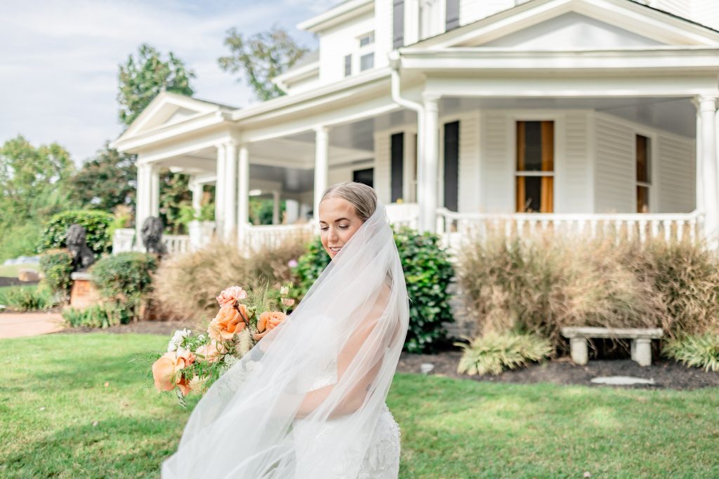 Bride in flowing veil holding colorful bouquet outside elegant white Southern home
