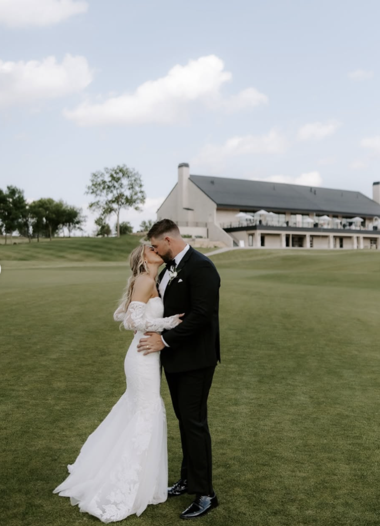 Newlyweds embrace on manicured golf course with modern venue building in background