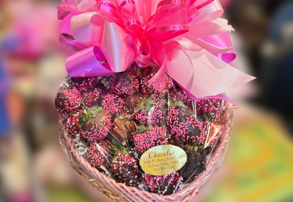 Chocolate-covered strawberries with pink and black sprinkles in a gift basket topped with vibrant pink ribbon bow