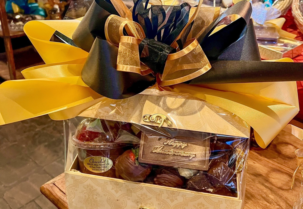 Gift basket wrapped in yellow and black ribbons containing chocolates, strawberries, and "Happy Anniversary" plaque