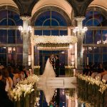 Grand ballroom ceremony with white floral chuppah and arched windows at twilight