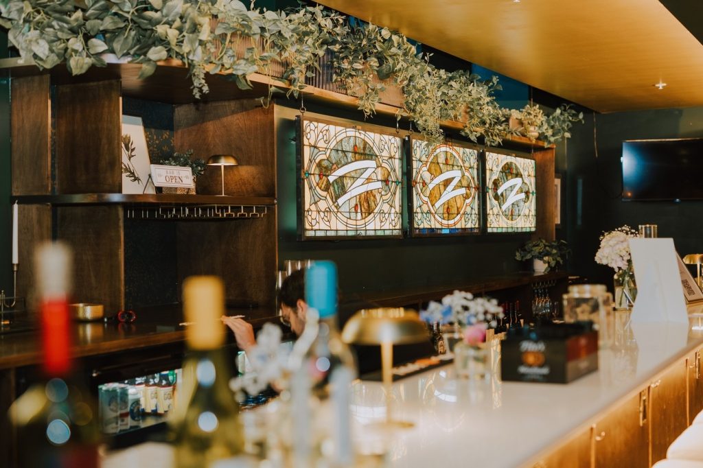 Upscale bar interior with illuminated stained glass panels, greenery garland, and dark wood shelving