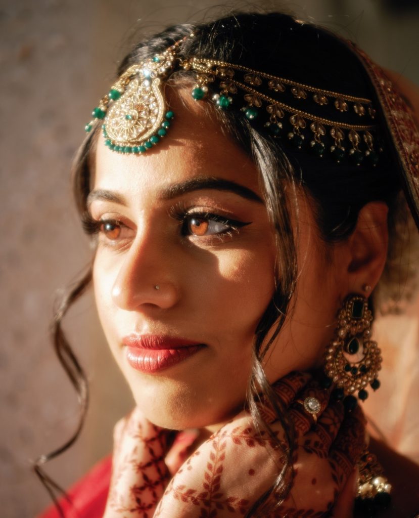 Bride wearing ornate gold and emerald South Asian jewelry with dramatic eye makeup and maang tikka headpiece