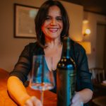 Woman in black dress smiling with wine bottle and glass at intimate dinner