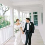 Bride and groom holding hands walking on covered porch at Southern-style venue