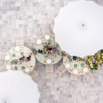 Overhead view of curved reception table arrangements with white umbrellas and floral centerpieces on gray stone patio