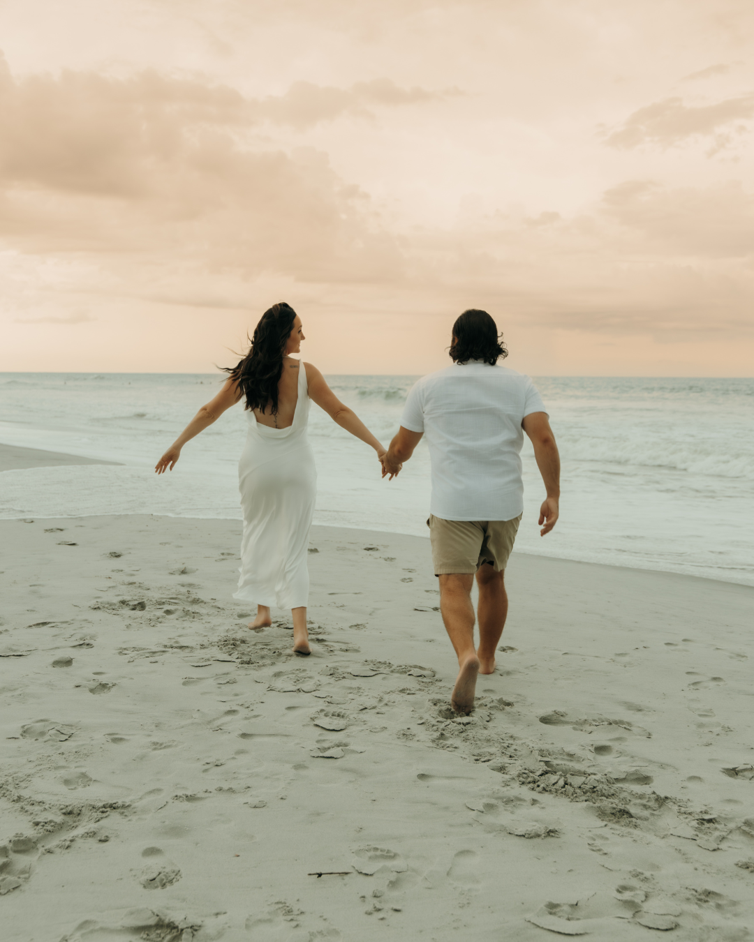 Bride and groom running barefoot along coastal Georgia shoreline at sunset