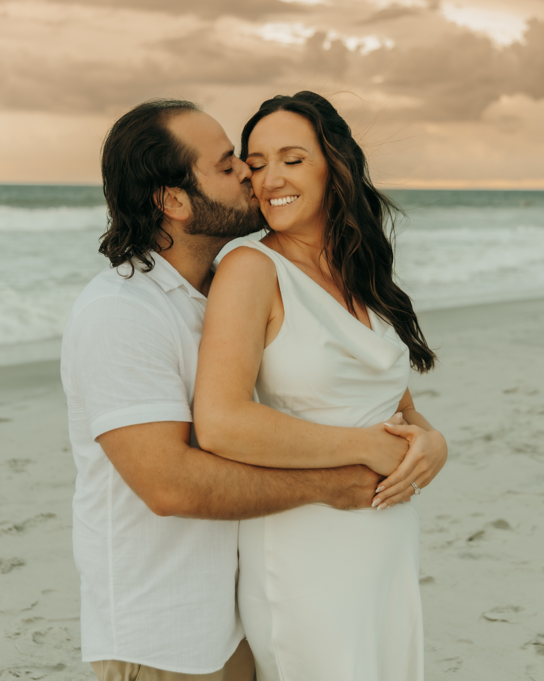 Couple embracing on coastal Georgia beach at sunset in casual white attire