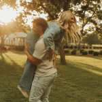 Couple embracing in golden hour sunlight on lawn with historic building behind them