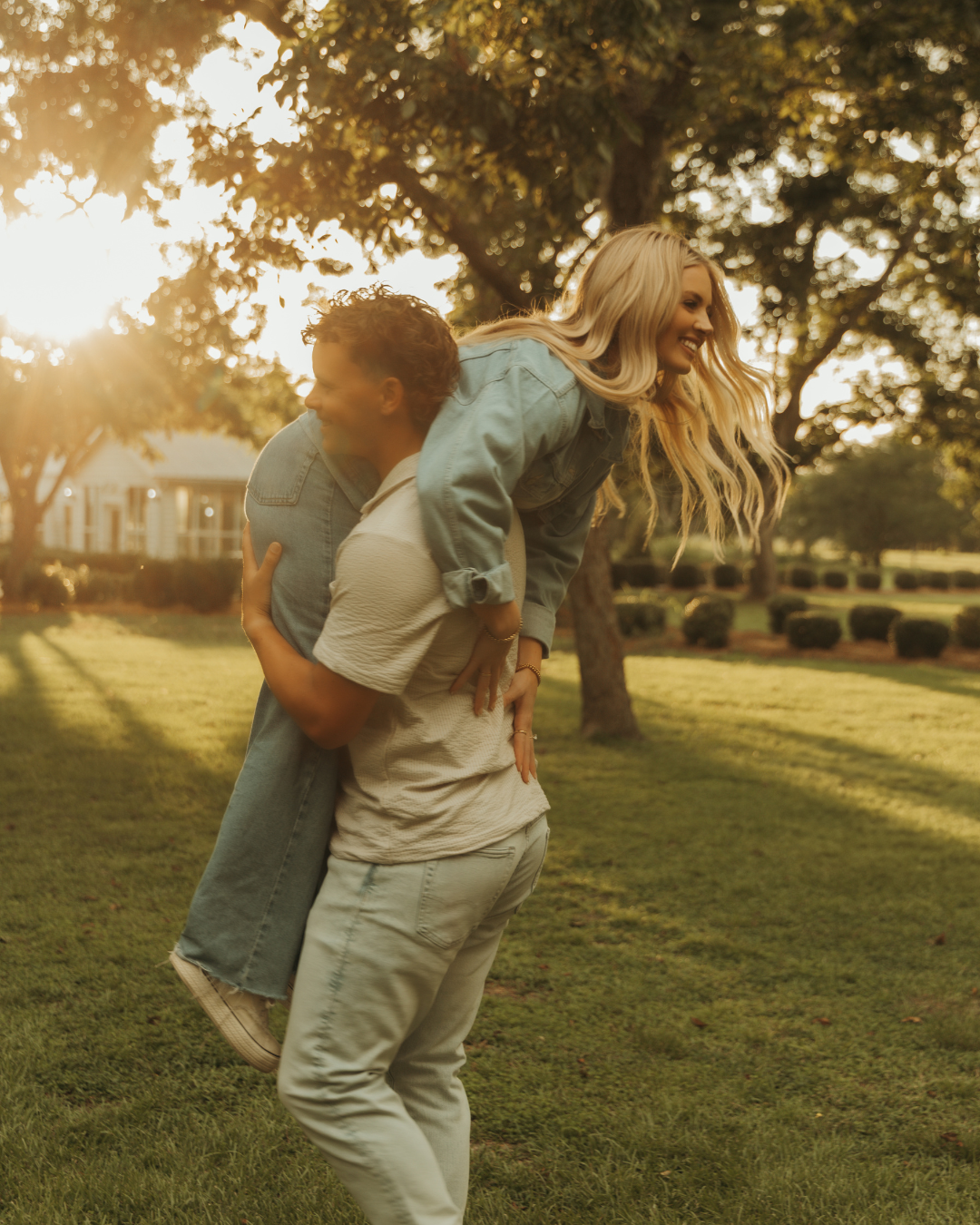 Couple embracing in golden hour sunlight on lawn with historic building behind them