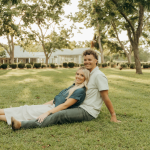 Engaged couple sitting together on lawn under oak trees in Savannah