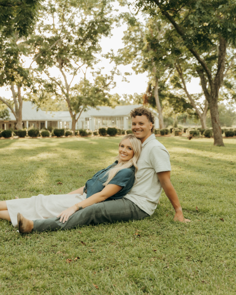 Engaged couple sitting together on lawn under oak trees in Savannah