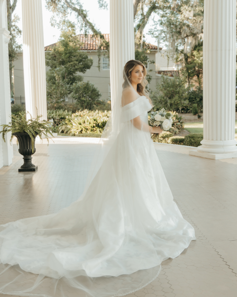 Bride twirling in flowing white gown on sunlit porch of Southern venue