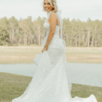 Bride in sparkly strapless gown with cathedral train twirling by lakeside with trees in background