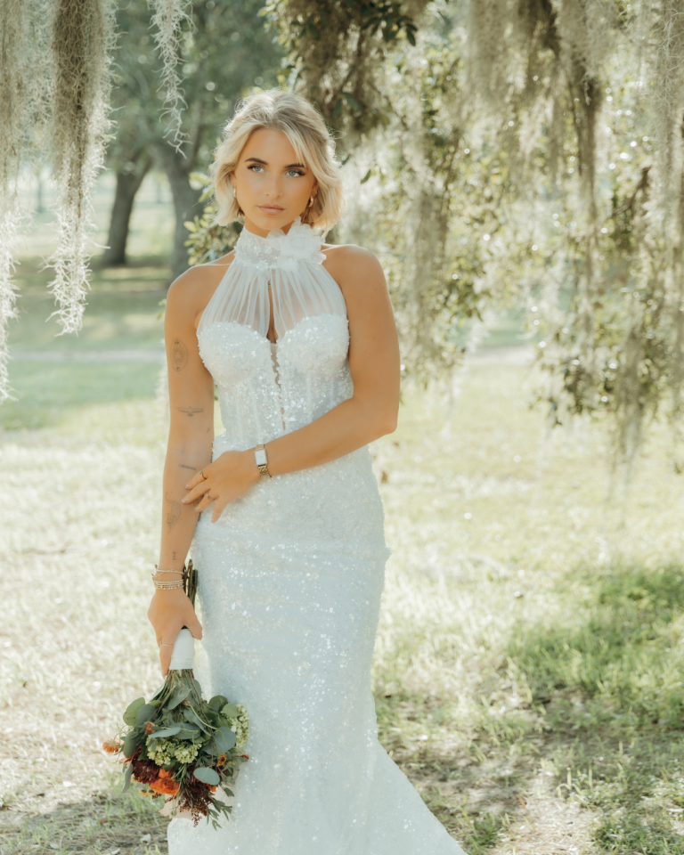 Bride in sequined halter wedding gown holding eucalyptus bouquet beneath Spanish moss-draped oak trees in Savannah