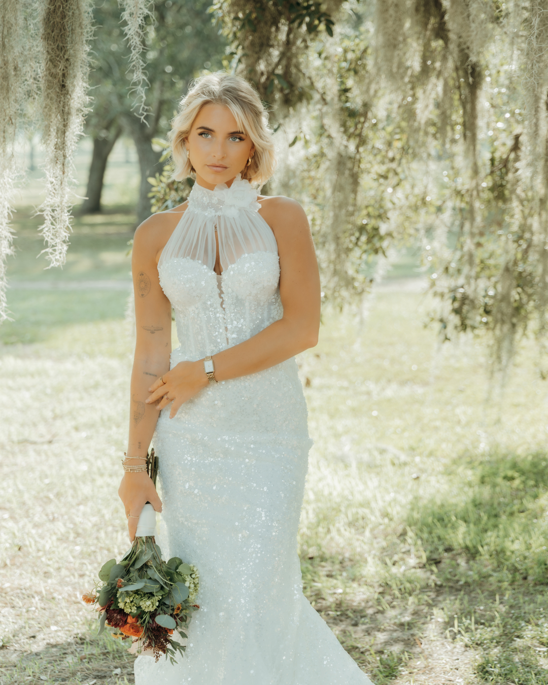Bride in sequined halter wedding gown holding eucalyptus bouquet beneath Spanish moss-draped oak trees in Savannah