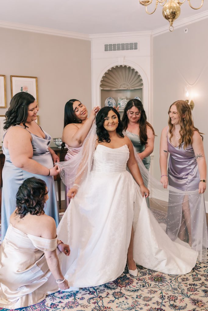 Bride getting ready with bridesmaids adjusting her veil in bridal suite at Brantwyn Estate in Wilmington, Delaware.