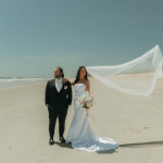 Newlyweds on coastal Georgia beach with bride's cathedral veil billowing in ocean breeze