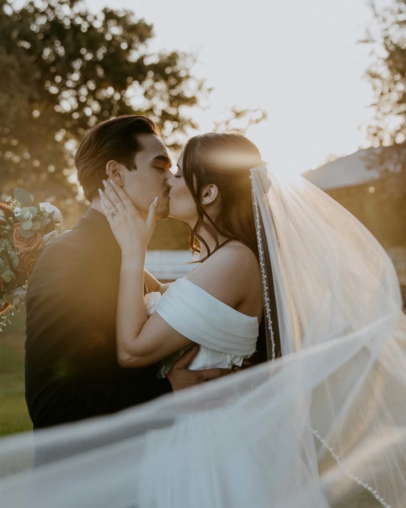 Bride and groom share intimate moment at golden hour with flowing veil