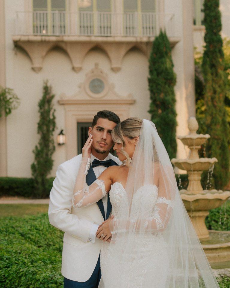 Newlyweds embrace in front of Mediterranean-style villa with cypress trees