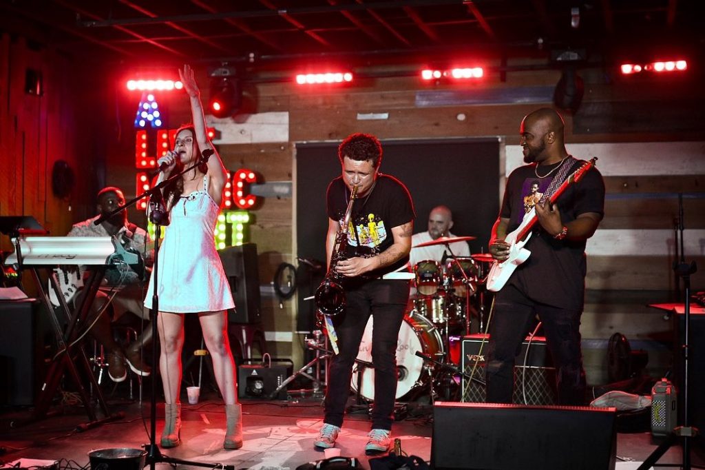 Live band performing at wedding reception with red stage lighting and rustic wooden backdrop