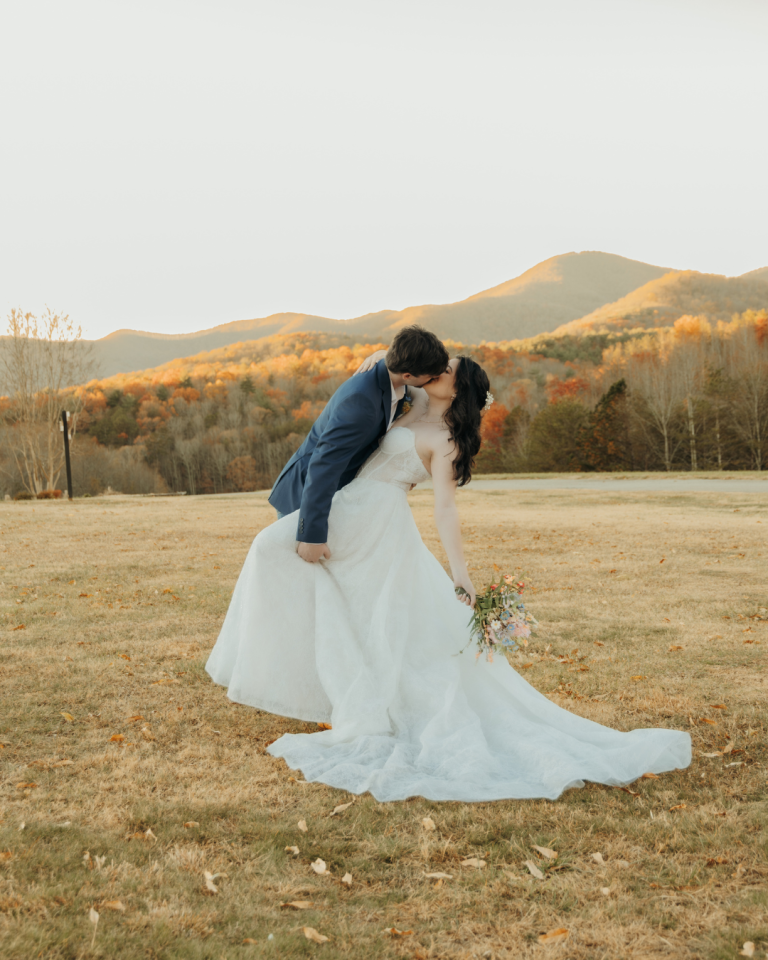 Newlyweds kissing in mountain field during golden hour with fall foliage